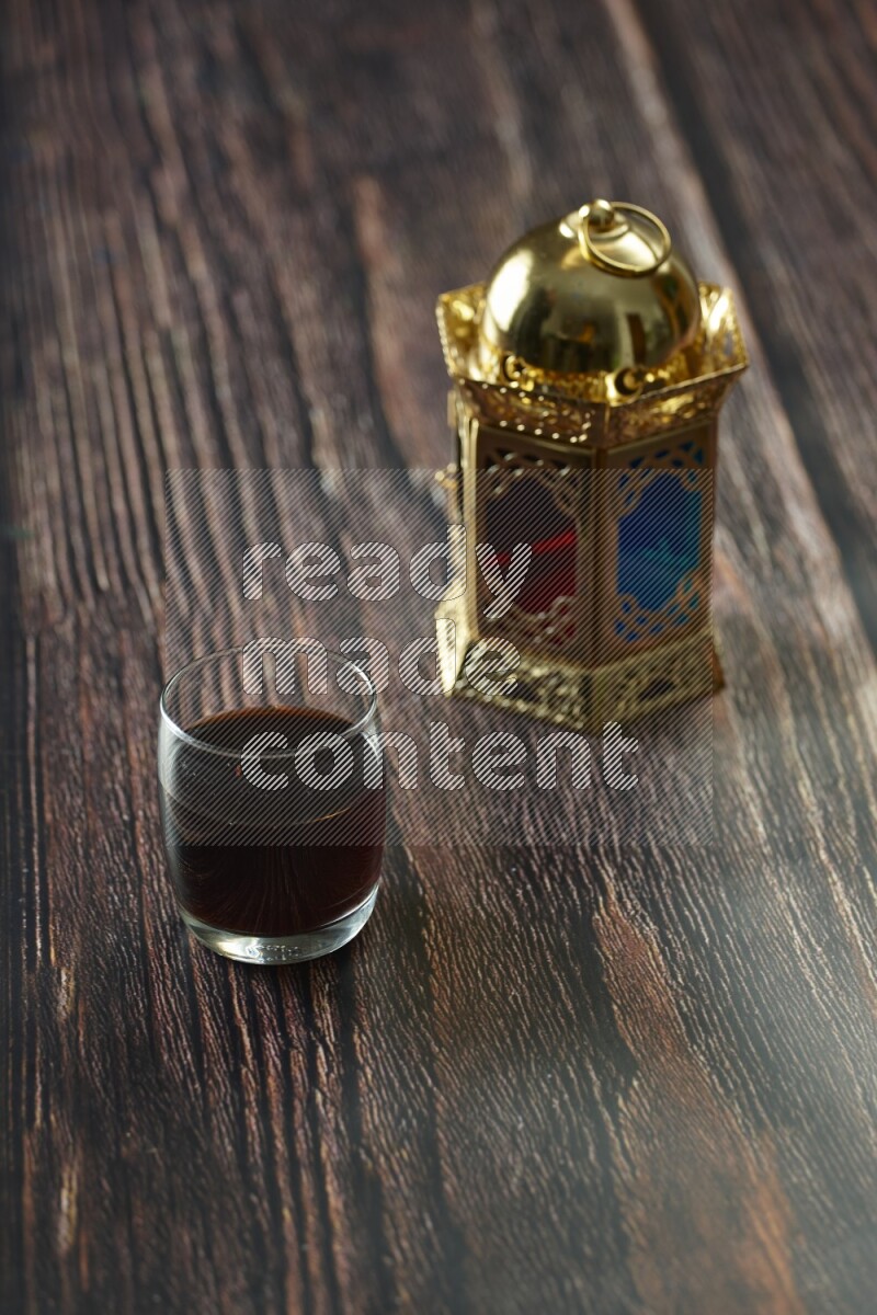 A golden lantern with different drinks, dates, nuts, prayer beads and quran on brown wooden background
