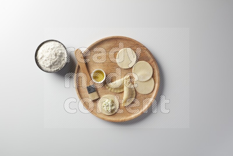 two closed sambosas and one open sambosa filled with cheese while flour, and oil with oil brush aside in a wooden dish on a white background