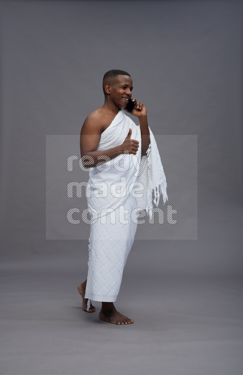 A man wearing Ehram Standing talking on phone on gray background