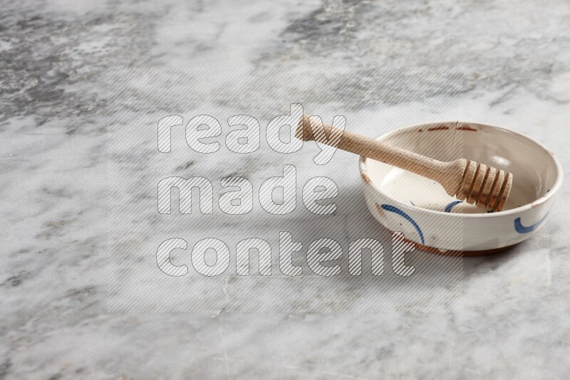 Multicolored pottery bowl with wooden honey dipper in it on grey marble background