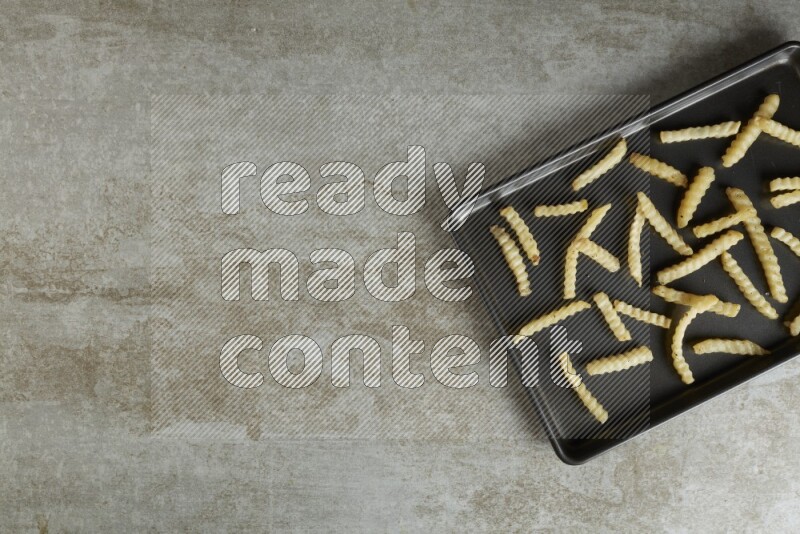 crinkle fries in a black stainless steel rectangle tray on grey textured counter top