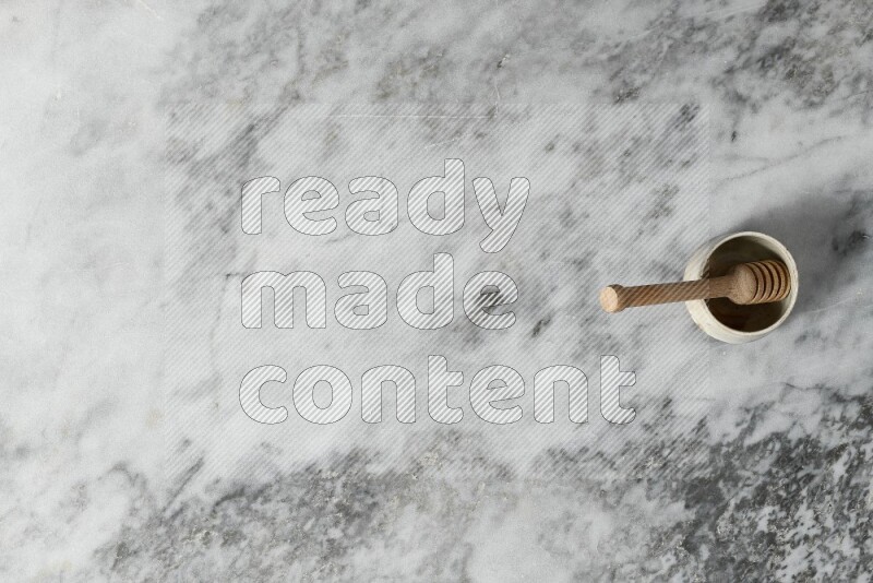 Black pottery bowl with wooden honey dipper in it on grey marble background