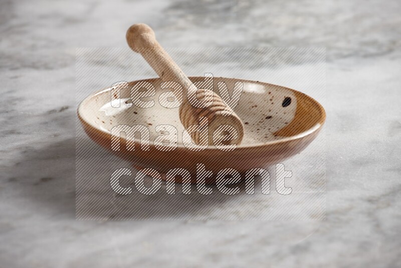 Multicolored pottery plate with wooden honey dipper in it on grey marble background