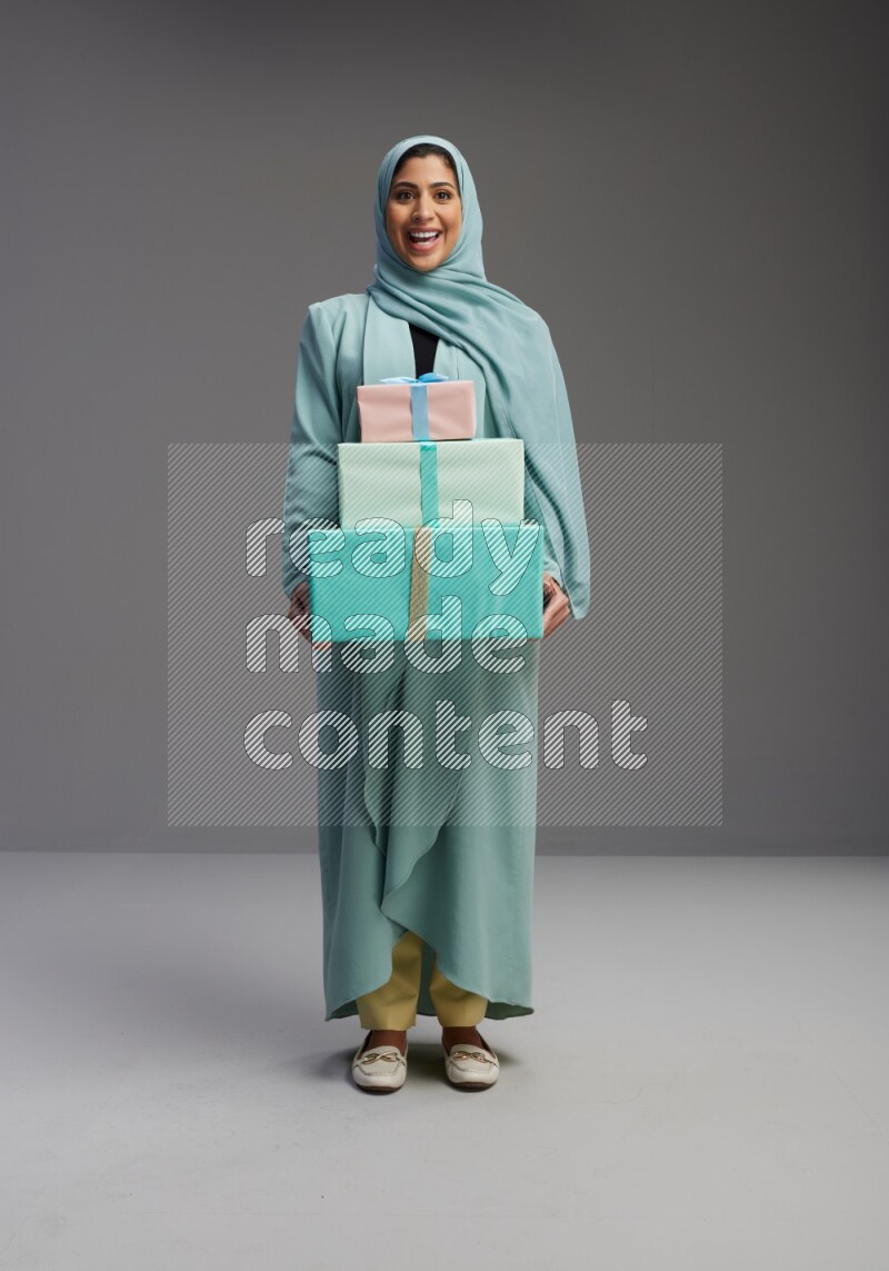 Saudi Woman wearing Abaya standing holding gift box on Gray background