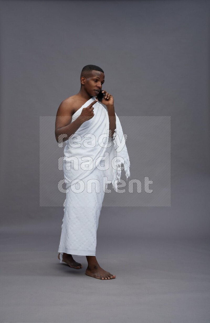 A man wearing Ehram Standing talking on phone on gray background