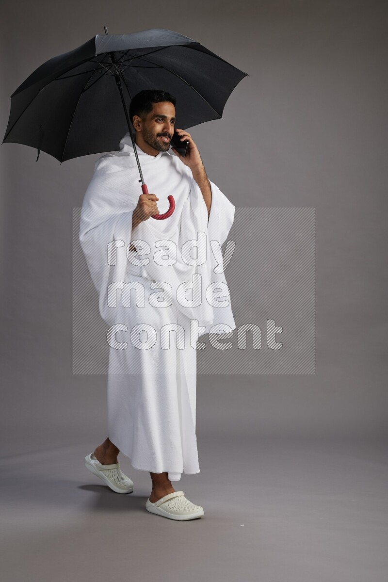 A man wearing Ehram Standing holding umbrella on gray background