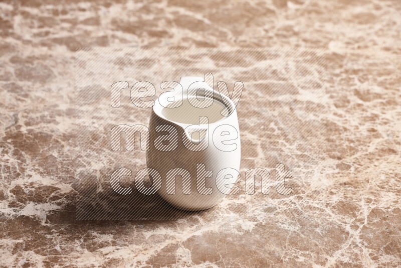 A ceramic milk jug on beige marble background