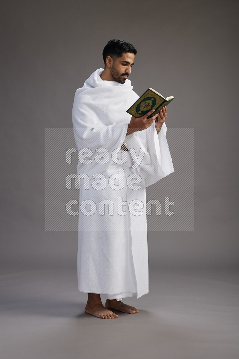 A man wearing Ehram Standing reading quran on gray background