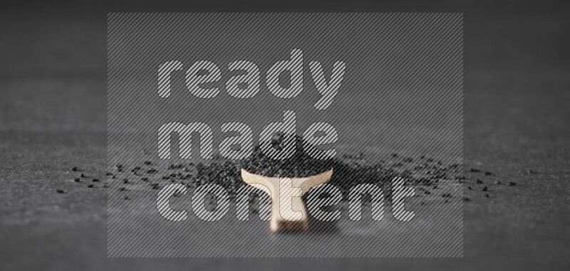 A wooden spoon full of black seeds and surrounded by seeds on a black flooring