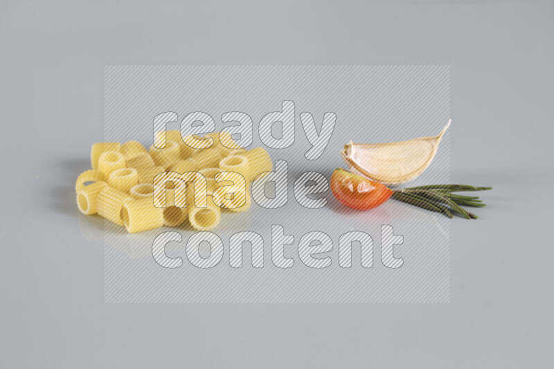 Raw pasta with different ingredients such as cherry tomatoes, garlic, onions, red chilis, black pepper, white pepper, bay laurel leaves, rosemary, cardamom and mushrooms on light blue background