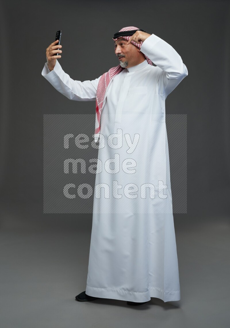 Saudi man with shomag Standing taking selfie on gray background