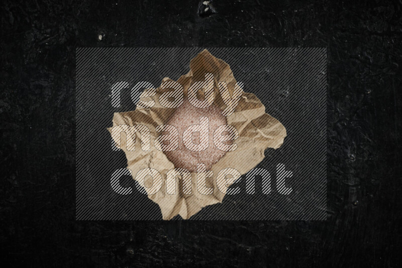 A crumpled piece of paper full of pink himalayan salt on black background
