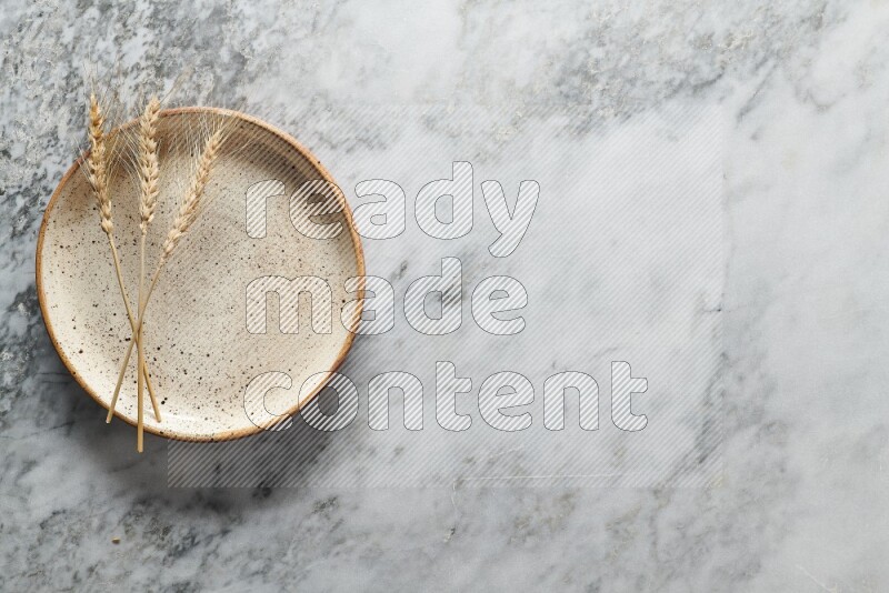Wheat stalks on multicolored pottery plate on grey marble background