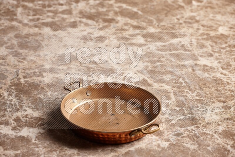 A small copper pan on beige marble background