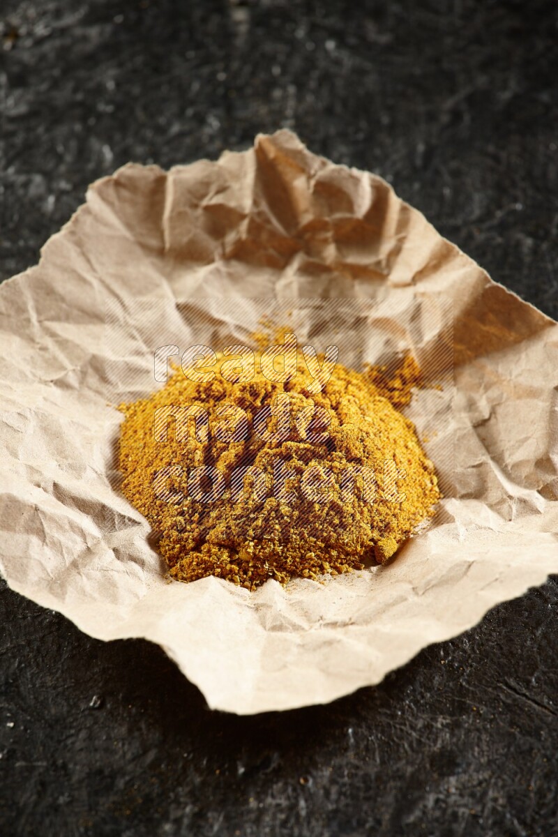 Turmeric powder in a crumpled piece of paper on textured black flooring