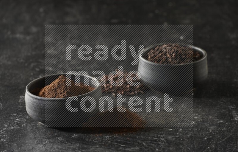 وعاءين من الفخار الأسود أحدهما ممتلئي بحبوب القرنفل والآخر ممتلئ ببودرة القرنفل على خلفية سوداء