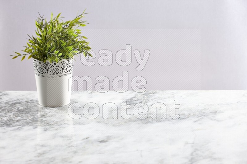 Green artificial plant in white decorative pot on grey marble background