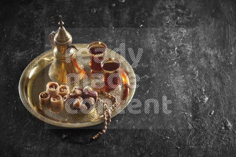 Oriental sweets with dates and a drink on a metal tray in a dark setup