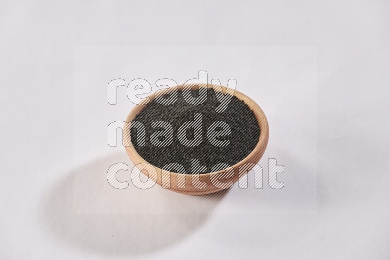 A wooden bowl full of black seeds on a white flooring