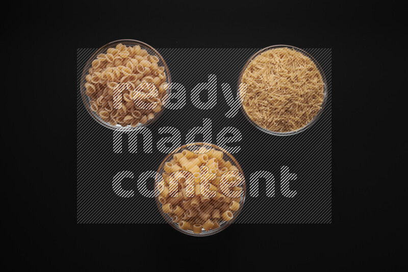 Different pasta types in glass bowls on black background