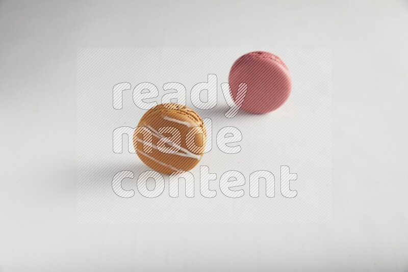 45º Shot of of two assorted Brown Irish Cream, and Pink Raspberry macarons on white background