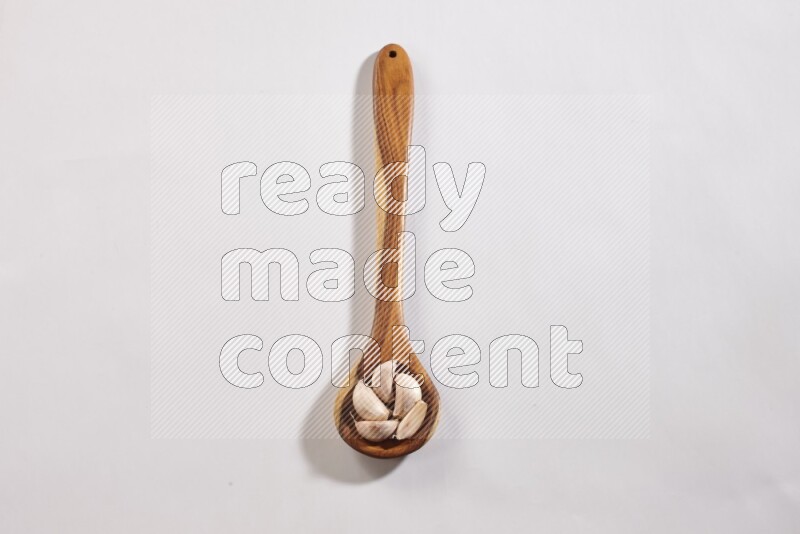 A wooden ladle full of garlic cloves with sprinkled powder on a white flooring