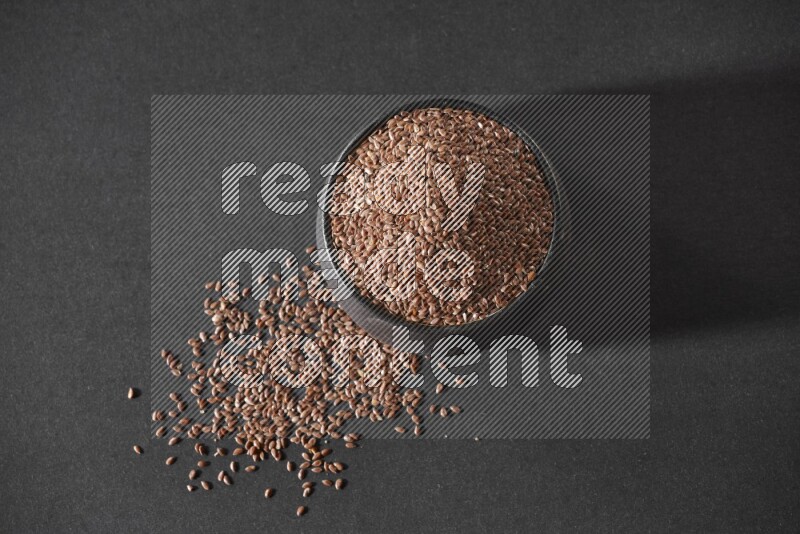 وعاء فخاري أسود ممتلئ بحبوب بذر الكتان محاط بالبذور على أرضية سوداء