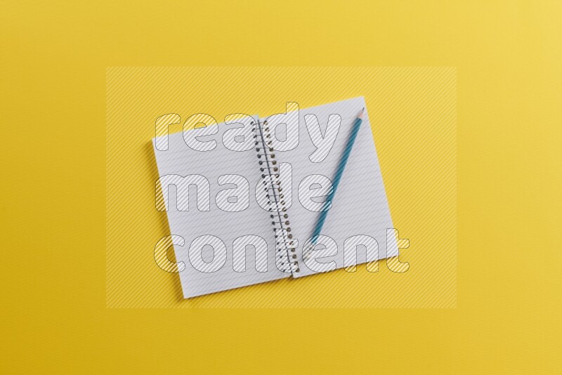 An open notebook with different school supplies on yellow background