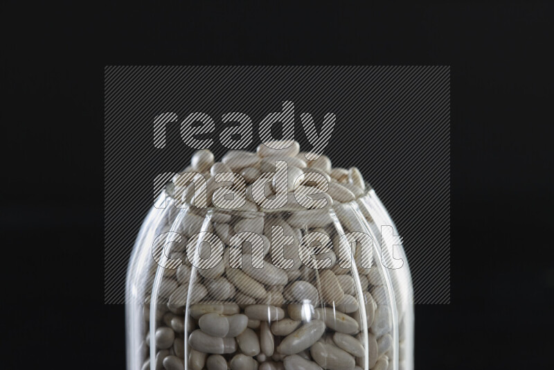 White beans in a glass jar on black background