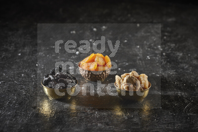 فواكه مجففة في أطباق معدنية علي خلفية سوداء خشبية