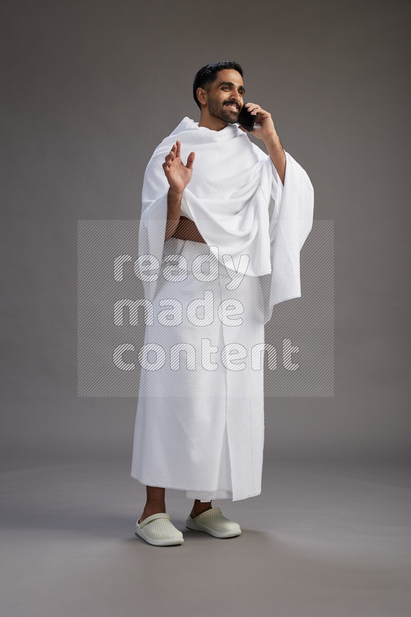 A man wearing Ehram Standing talking on phone on gray background