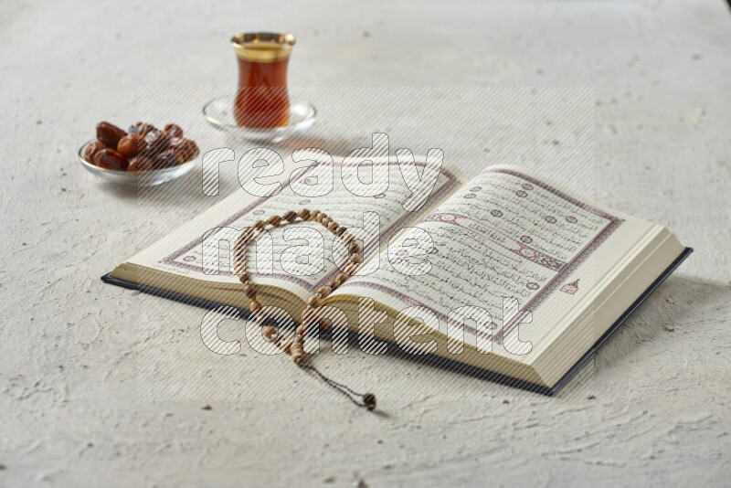 Quran with dates, prayer beads and different drinks all placed on textured white background