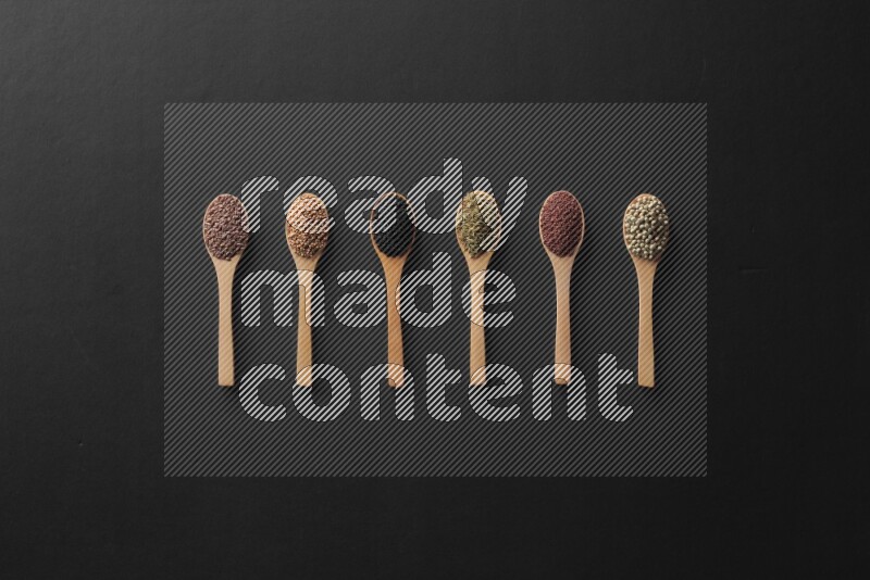 الفلفل الأسود وحبوب الخردل وحبة البركة وحب الرشاد والكمون و حبوب الكتان في معالق خشبية علي خلفية سوداء