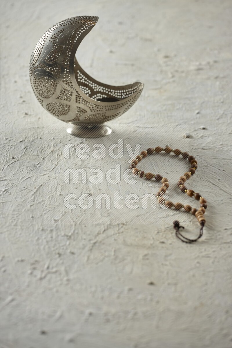 A silver lantern with different drinks, dates, nuts, prayer beads and quran on textured white background