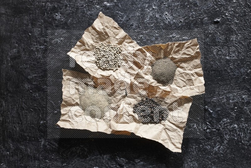 قطع من الورق ممتلئة بحبوب وبودرة الفلفل الأسود والأبيض على أرضية سوداء