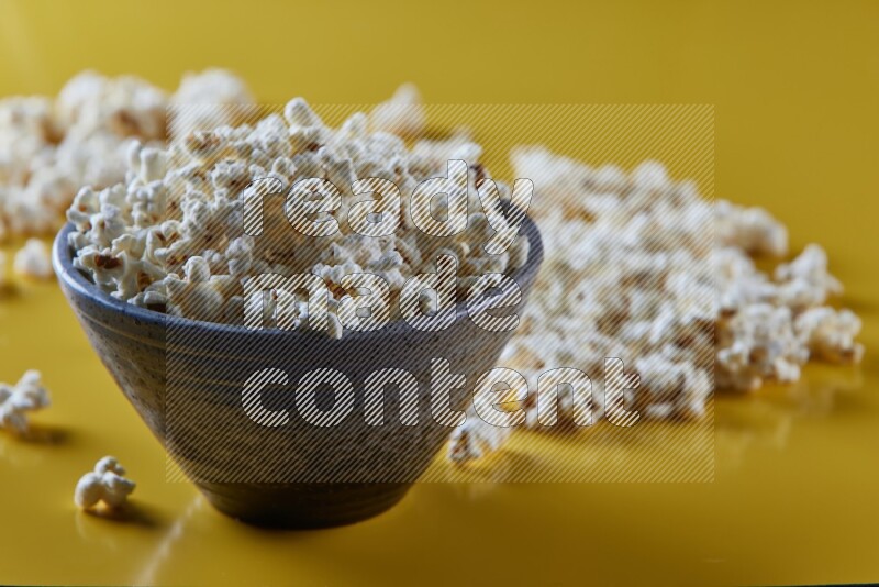 A multicolored pottery bowl full of popcorn with popcorn beside it on a yellow background in different angles