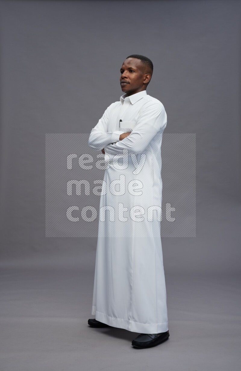 Saudi man wearing thob standing with crossed arms on gray background