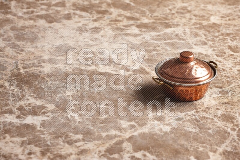 A small copper pot on beige marble background