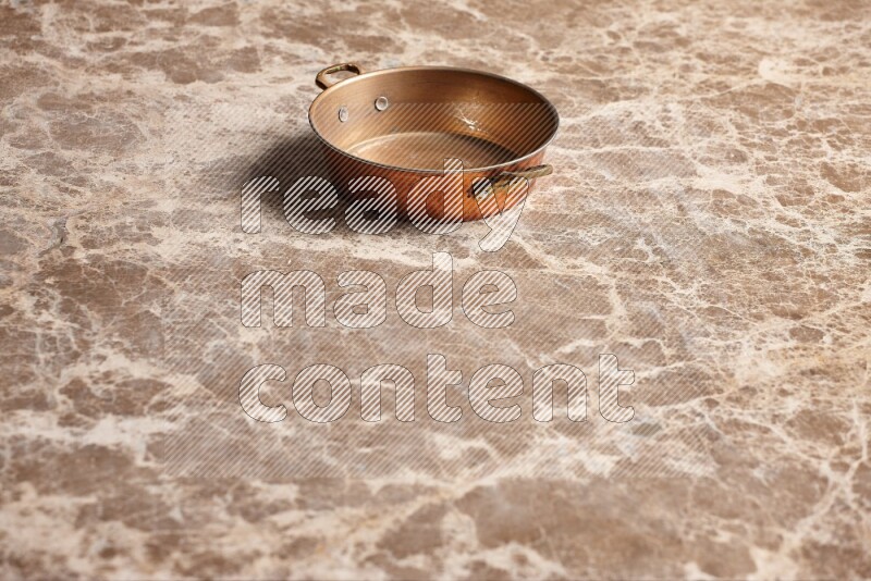 A small copper pan on beige marble background