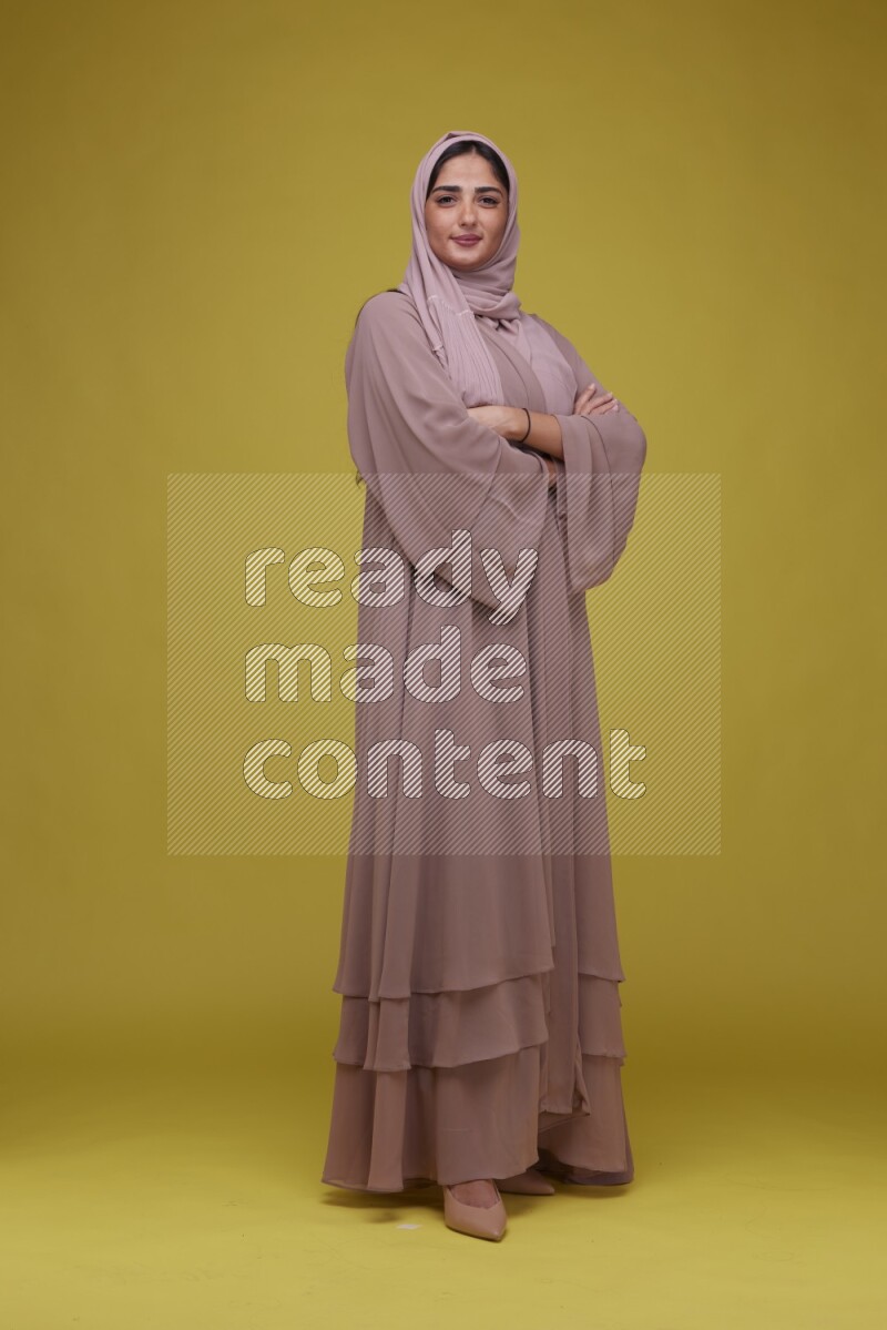A woman Posing on a Yellow Background wearing Brown Abaya with Hijab