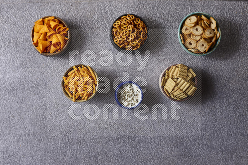 Assorted snacks in pottery bowls on grey background