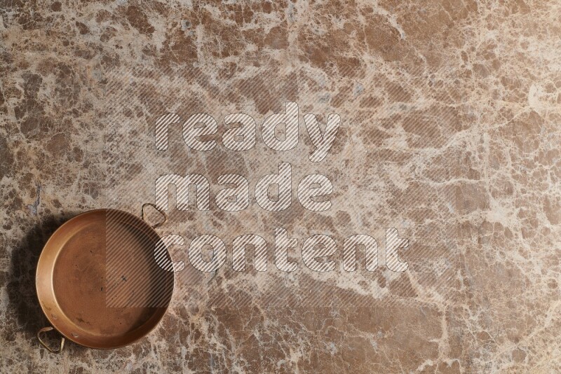A small copper pan on beige marble background