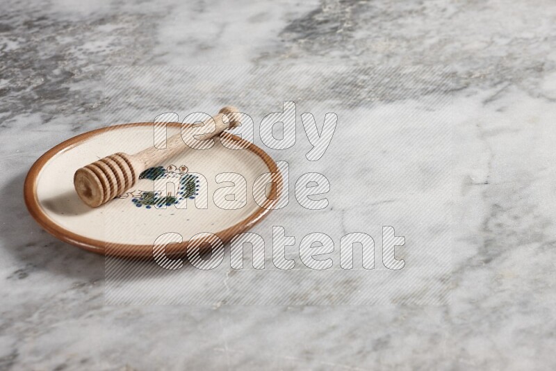 Decorative pottery plate with wooden honey dipper in it on grey marble background