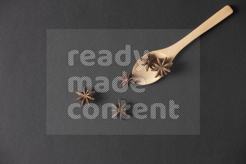 اليانسون النجمي في ملعقة خشبية فوق اليانسون النجمي الذي يغطي الإطار على أرضية سوداء