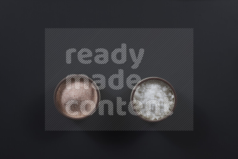 2 وعاء فخاري احدهمها ممتلئ بملح الهيمالايا والأخر بالملح الأبيض على خلفية سوداء