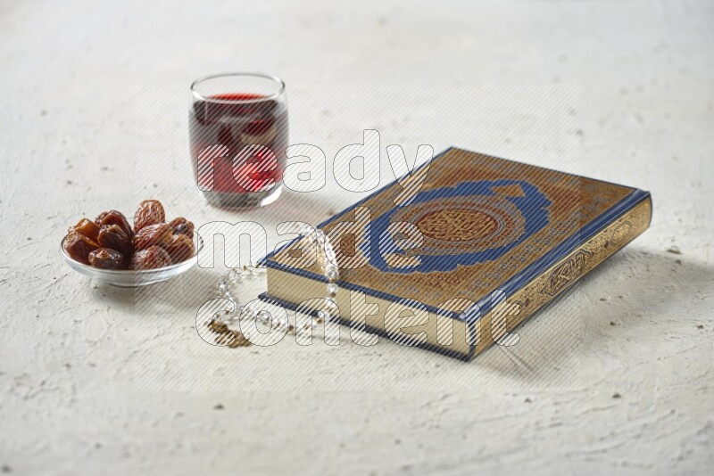 Quran with dates, prayer beads and different drinks all placed on textured white background