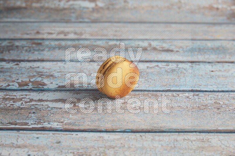 45º Shot of Yellow Crème Brulée macaron on light blue wooden background