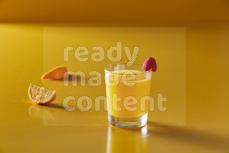 glass of orange juice with berry on yellow background