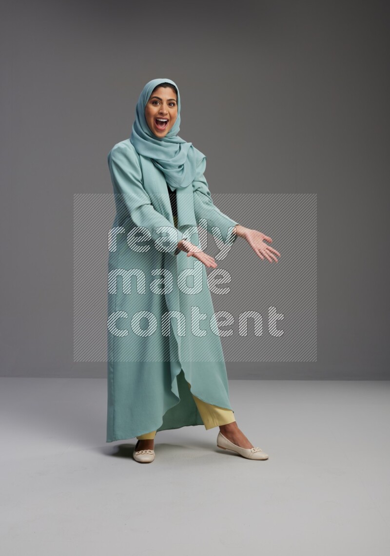 Saudi Woman wearing Abaya standing interacting with the camera on Gray background