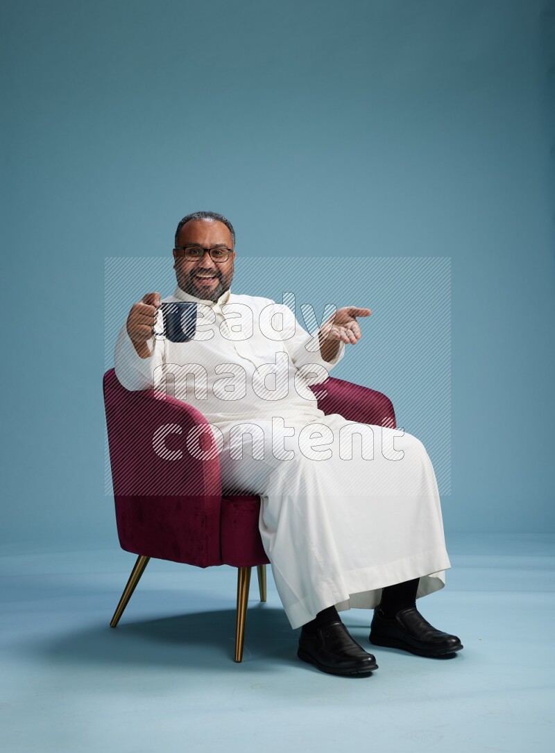Saudi Man without shimag sitting on chair drinking coffee on blue background